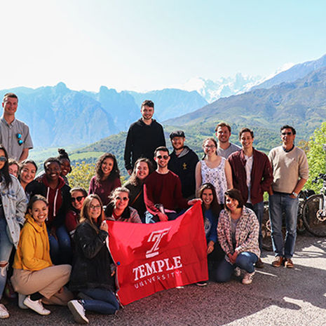 Mountains in the background, a group of Temple students holding a Temple cherry flag.
