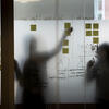 Person adding a post it note to a clear glass wall